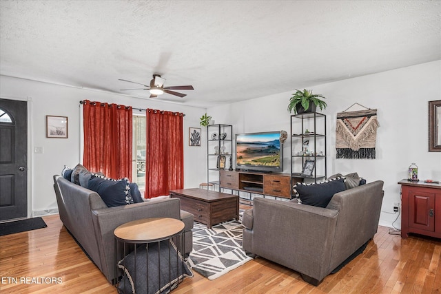 living room with ceiling fan, light wood-type flooring, and a textured ceiling