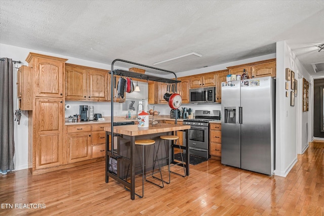 kitchen with a center island, stainless steel appliances, wooden counters, a textured ceiling, and light wood-type flooring