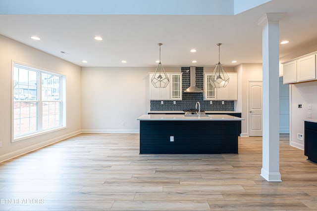 kitchen with wall chimney exhaust hood, sink, tasteful backsplash, hanging light fixtures, and a kitchen island with sink