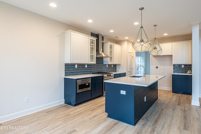 kitchen featuring white cabinetry, a kitchen island with sink, wall chimney exhaust hood, and appliances with stainless steel finishes