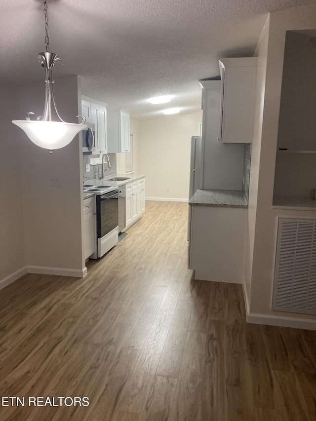 kitchen featuring pendant lighting, white cabinets, hardwood / wood-style flooring, a textured ceiling, and appliances with stainless steel finishes