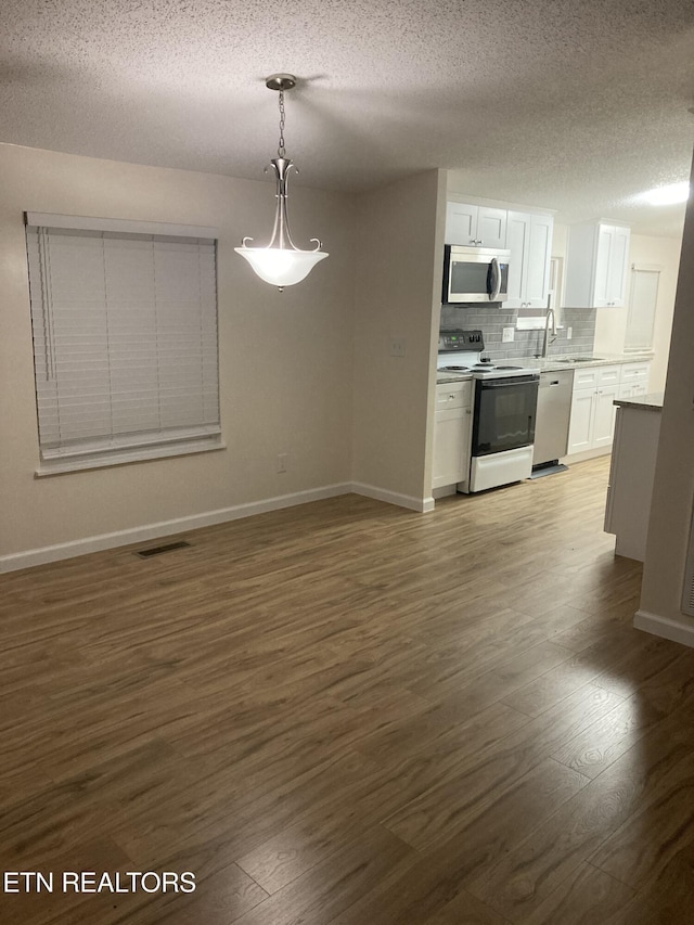 kitchen featuring dark wood-type flooring, a textured ceiling, appliances with stainless steel finishes, decorative light fixtures, and white cabinetry