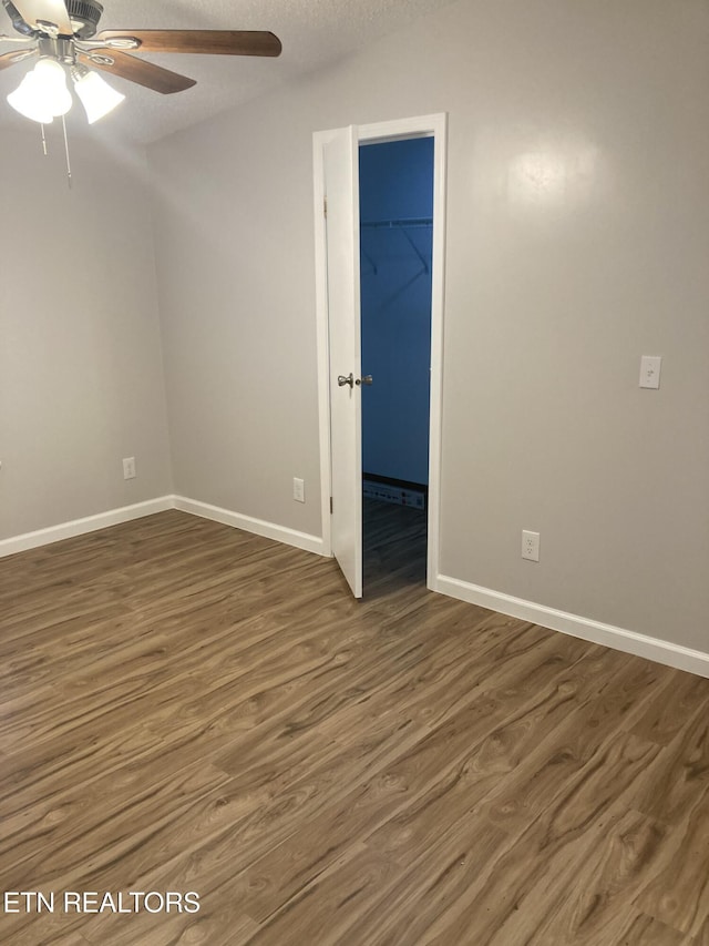 unfurnished bedroom featuring dark hardwood / wood-style flooring, a walk in closet, a textured ceiling, ceiling fan, and a closet