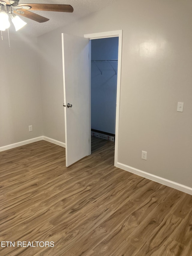 unfurnished bedroom with ceiling fan, a spacious closet, a textured ceiling, dark hardwood / wood-style flooring, and a closet