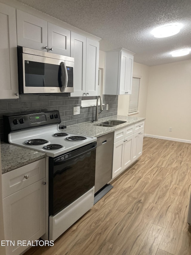 kitchen featuring stainless steel appliances, white cabinetry, light hardwood / wood-style floors, and sink