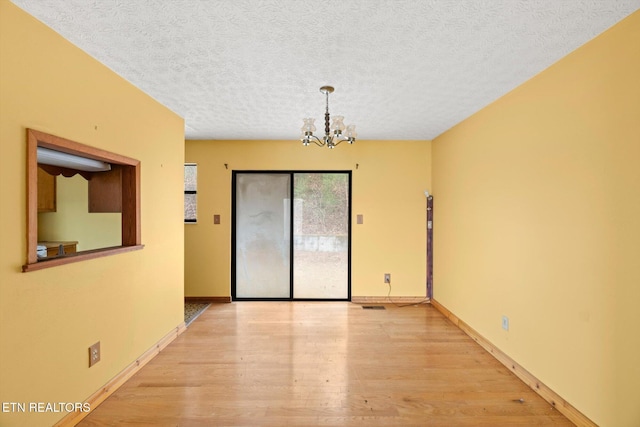 unfurnished room featuring light hardwood / wood-style floors, a textured ceiling, and a chandelier