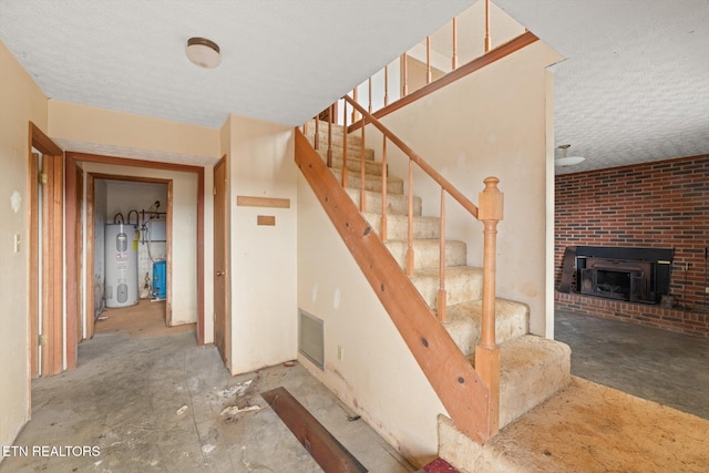 stairway with electric water heater, a fireplace, and a textured ceiling