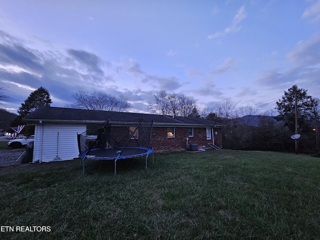 back house at dusk with a lawn and a trampoline