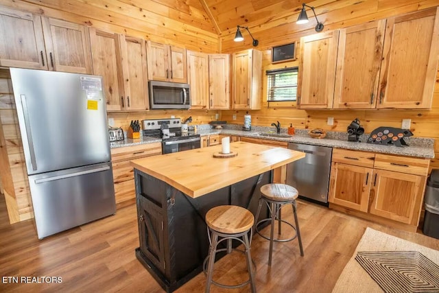 kitchen featuring a kitchen bar, wooden counters, a kitchen island, appliances with stainless steel finishes, and sink