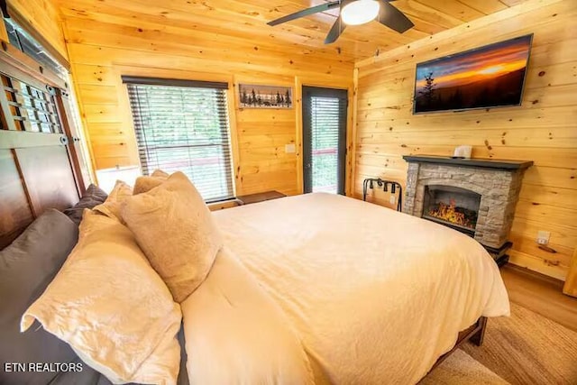 bedroom featuring wooden walls, wooden ceiling, hardwood / wood-style floors, ceiling fan, and a stone fireplace