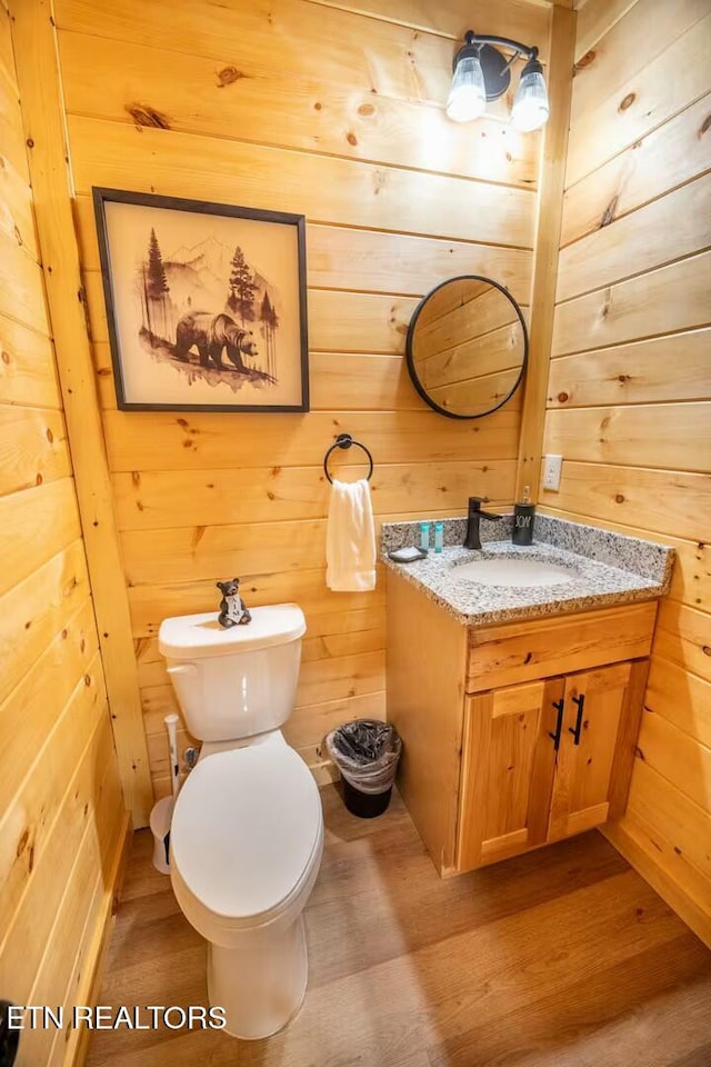 bathroom featuring toilet, hardwood / wood-style flooring, wooden walls, and vanity