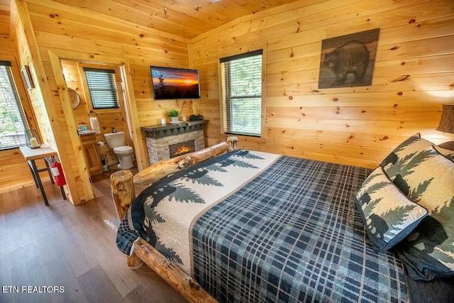 bedroom featuring a stone fireplace, ensuite bathroom, wooden walls, and multiple windows