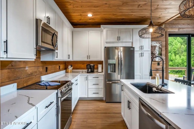 kitchen with appliances with stainless steel finishes, sink, decorative light fixtures, white cabinets, and wood walls