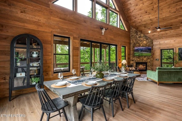 dining area featuring a fireplace, wood walls, plenty of natural light, and high vaulted ceiling