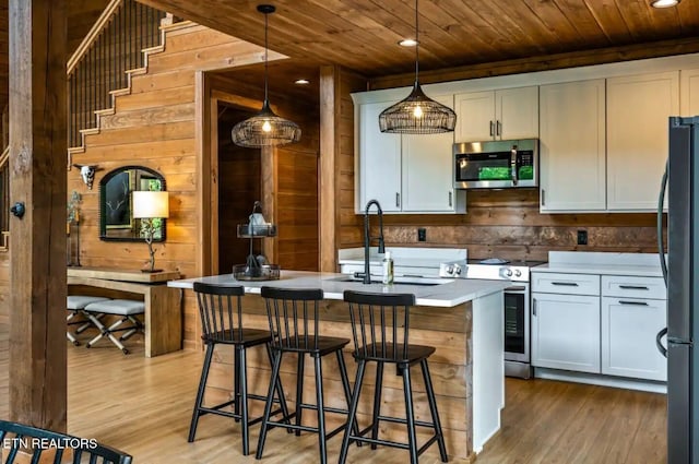 kitchen with pendant lighting, stainless steel appliances, light hardwood / wood-style floors, and an island with sink