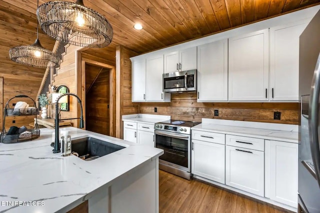 kitchen with light stone countertops, stainless steel appliances, light hardwood / wood-style floors, decorative light fixtures, and white cabinets