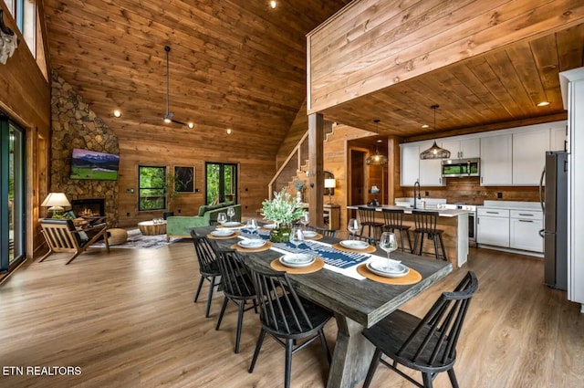 dining space featuring wooden ceiling, high vaulted ceiling, light hardwood / wood-style floors, wooden walls, and a fireplace