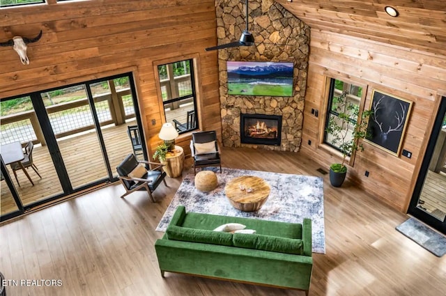 living room with a high ceiling, hardwood / wood-style flooring, a stone fireplace, and wood walls