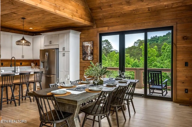 dining room with sink, vaulted ceiling, wooden walls, wood ceiling, and light wood-type flooring