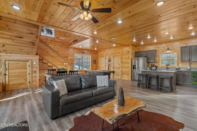 living room featuring wood-type flooring, wooden walls, ceiling fan, and wood ceiling