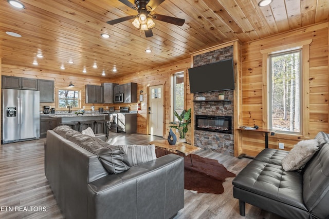 living room with a fireplace, light wood-type flooring, ceiling fan, wood walls, and wood ceiling