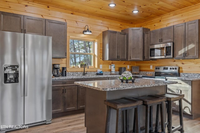 kitchen featuring appliances with stainless steel finishes, light hardwood / wood-style floors, a kitchen island, and light stone countertops