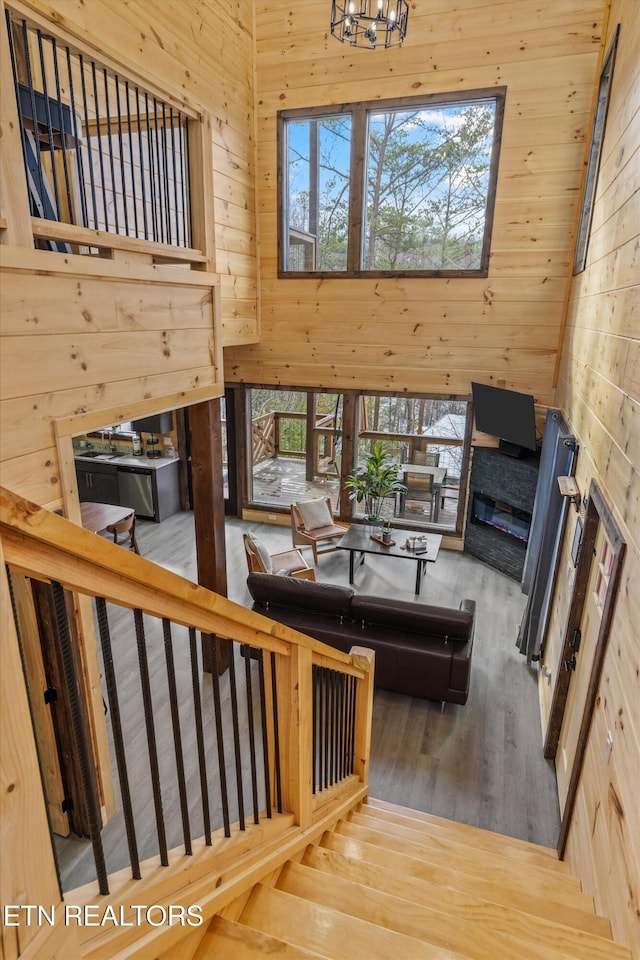 stairs with an inviting chandelier, wooden walls, a towering ceiling, and wood-type flooring