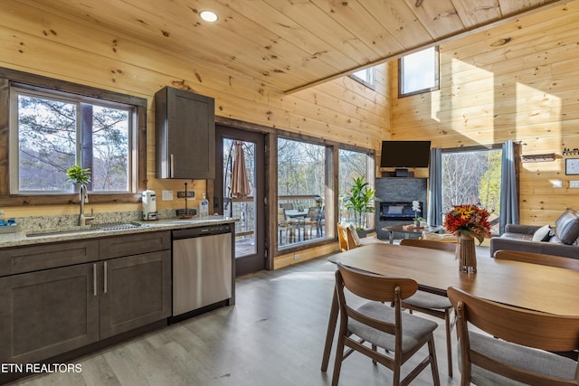 kitchen with sink, dishwasher, light stone counters, wood walls, and dark brown cabinetry