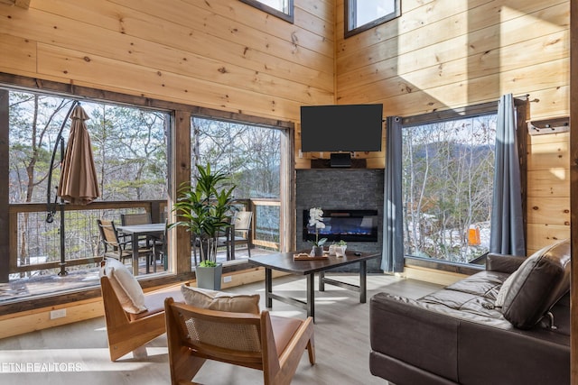 living room with a high ceiling, wooden walls, a fireplace, and light hardwood / wood-style floors