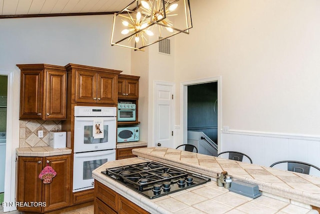 kitchen with an inviting chandelier, tile countertops, decorative light fixtures, white appliances, and a breakfast bar