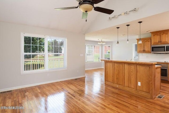 kitchen featuring vaulted ceiling, a kitchen island, decorative light fixtures, light hardwood / wood-style floors, and stainless steel appliances