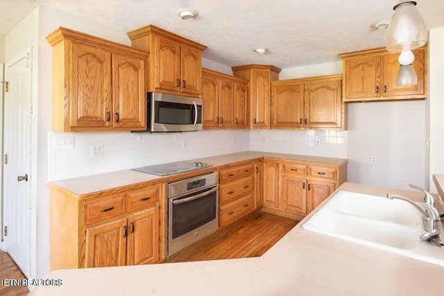 kitchen featuring appliances with stainless steel finishes, light wood-type flooring, backsplash, sink, and hanging light fixtures