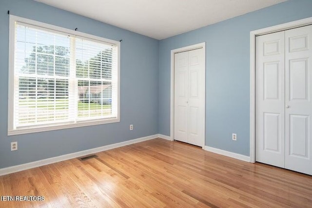 unfurnished bedroom featuring two closets and light wood-type flooring