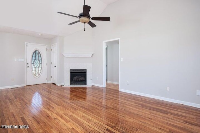 unfurnished living room featuring hardwood / wood-style floors, vaulted ceiling, ceiling fan, and a tiled fireplace