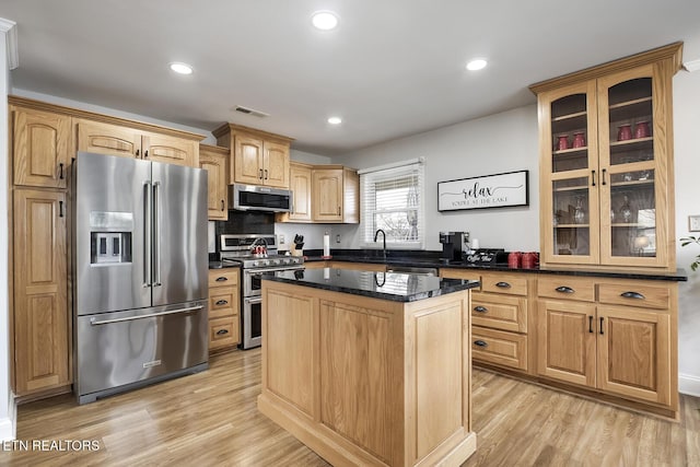 kitchen with stainless steel appliances, light wood-type flooring, dark stone counters, a kitchen island, and sink