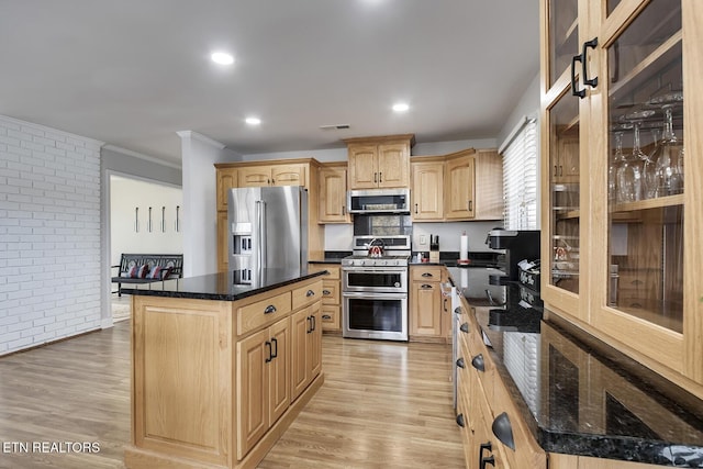 kitchen featuring light brown cabinetry, brick wall, a kitchen island, crown molding, and appliances with stainless steel finishes