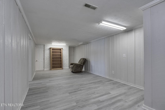 basement with wooden walls, a textured ceiling, crown molding, and light hardwood / wood-style flooring