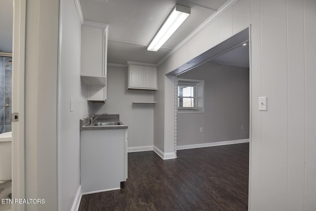 kitchen with dark wood-type flooring, white cabinetry, crown molding, and sink