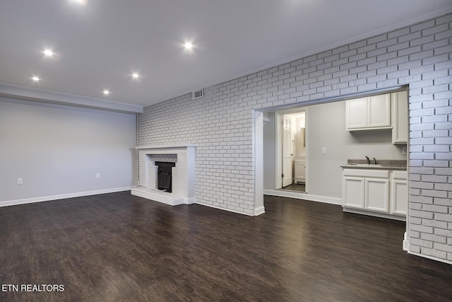 unfurnished living room featuring sink, a fireplace, brick wall, and dark hardwood / wood-style floors