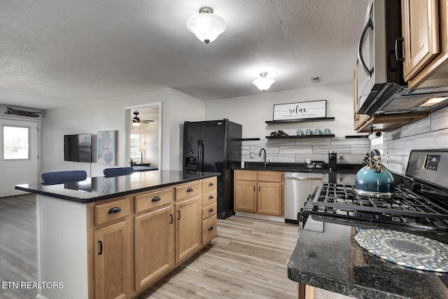 kitchen with appliances with stainless steel finishes, light wood-type flooring, a center island, a textured ceiling, and backsplash