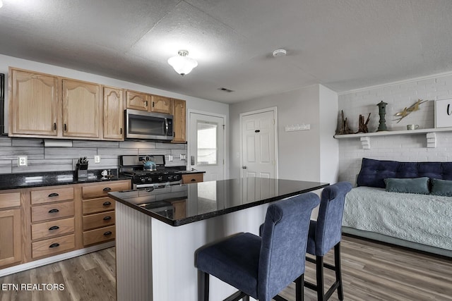 kitchen with stainless steel appliances, a textured ceiling, a kitchen bar, hardwood / wood-style floors, and decorative backsplash