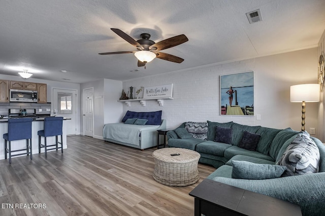 living room with brick wall, a textured ceiling, ceiling fan, and hardwood / wood-style flooring