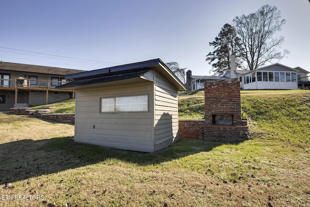 view of outdoor structure featuring an outdoor brick fireplace and a lawn