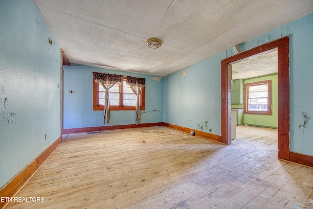 spare room with a textured ceiling, light wood-type flooring, and a wealth of natural light