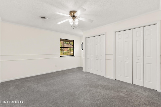 unfurnished bedroom with dark colored carpet, crown molding, ceiling fan, multiple closets, and a textured ceiling