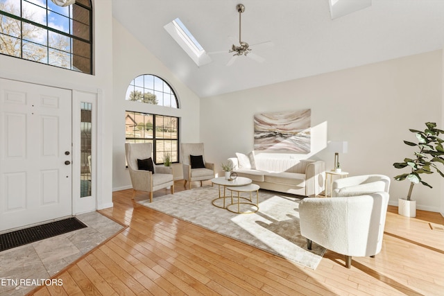 living room with a towering ceiling, a skylight, ceiling fan, and light hardwood / wood-style flooring