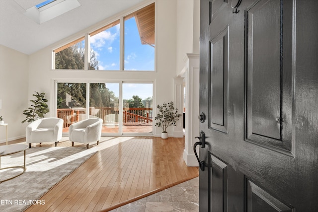 foyer featuring a high ceiling, a skylight, a wealth of natural light, and light wood-type flooring