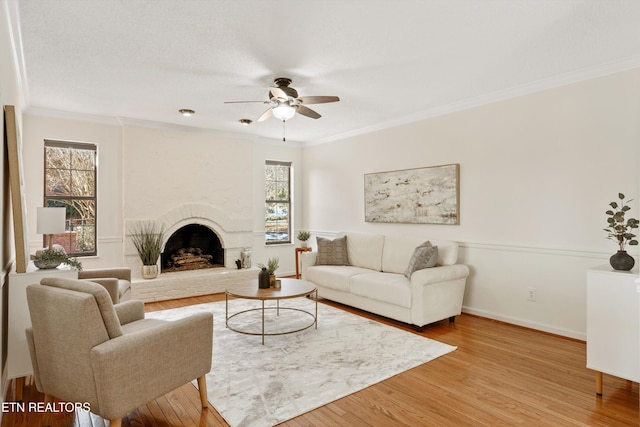 living room with a large fireplace, light hardwood / wood-style flooring, a wealth of natural light, and crown molding