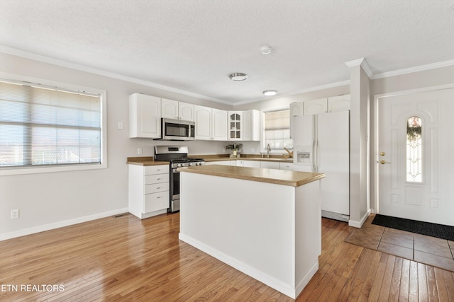 kitchen featuring stainless steel appliances, a kitchen island, light wood-type flooring, white cabinetry, and ornamental molding