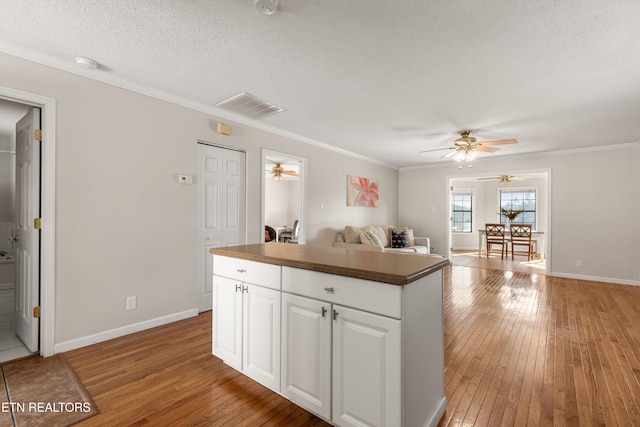 kitchen featuring white cabinets, a textured ceiling, hardwood / wood-style floors, ornamental molding, and a kitchen island